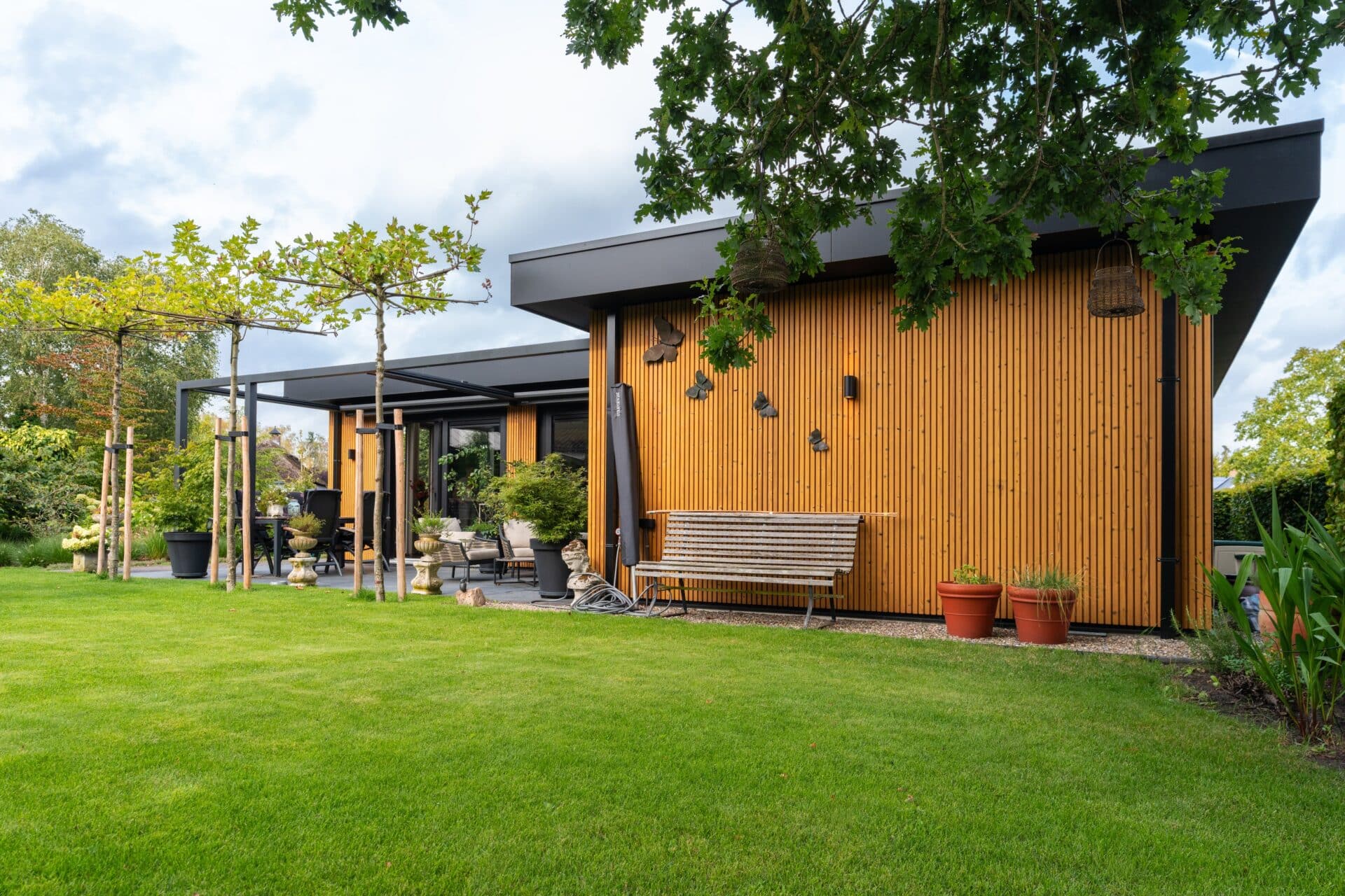 Moderne mantelzorgwoning van Solilux in Loenen met verticale gevelbekleding in warme houttinten, plat dak en overdekt terras, gelegen in een ruime, groene tuin.
