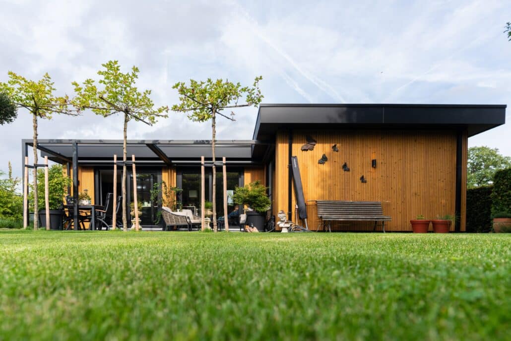 Moderne mantelzorgwoning van Solilux in Loenen met verticale gevelbekleding in warme houttinten, plat dak en overdekt terras, gelegen in een ruime, groene tuin.