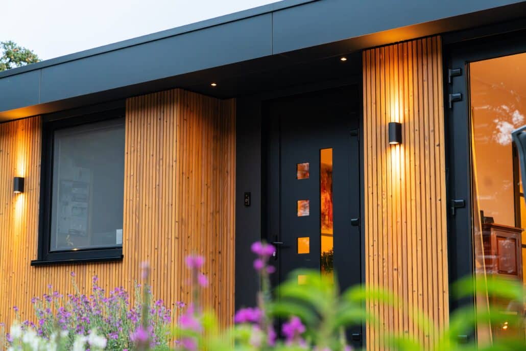 Mantelzorgwoning van Solilux in de Achterhoek in avondlicht, met verticale gevelbekleding in warme houttinten, schuifpui en sfeervolle wandverlichting, met zicht over het landelijke buitengebied.