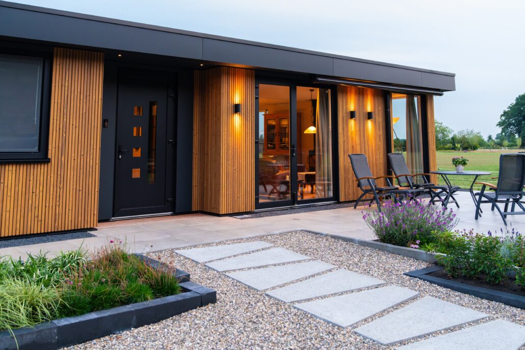 Mantelzorgwoning van Solilux in de Achterhoek in avondlicht, met verticale gevelbekleding in warme houttinten, schuifpui en sfeervolle wandverlichting, met zicht over het landelijke buitengebied.